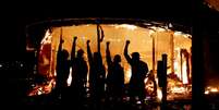 Manifestantes posam do lado de fora de loja de bebidas em chamas nos Estados Unidos  Foto: Reuters / BBC News Brasil