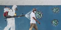 Homem passa pela frente de um grafite, enquanto um funcionário do serviço de saúde borrifa um spray contra o coronavírus. 12/6/2020. REUTERS/Sergio Moraes  Foto: Reuters