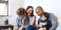 Casal multiracial, com dois filhos, sentados em um sofá  Foto: Shutterstock / Alto Astral