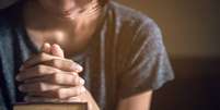 Mulher com as mãos fechadas, orando sobre uma bíblia  Foto: Shutterstock / Alto Astral