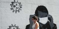 Mulher passa por grafite do presidente Jair Bolsonaro ajustando sua máscara protetora e em forma de vírus, em meio ao surto de Covid-19 no Rio de Janeiro. 02/07/2020. REUTERS/Sergio Moraes  Foto: Reuters