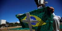 Ativista coloca bandeira do Brasil pintada com cruzes sobre cruz durante ato em homenagem a vítimas da Covid-19 em Brasília
14/07/2020
REUTERS/Adriano Machado  Foto: Reuters