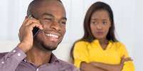 Homem falando no celular e mulher desconfiada  Foto: Shutterstock / Alto Astral