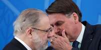 O presidente Jair Bolsonaro cobre a boca e fala algo no ouvido do PGR Augusto Aras  Foto: Reuters / BBC News Brasil