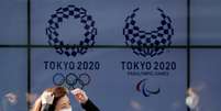 Mulher com máscara de proteção caminha em frente aos logos da Olimpíada e da Paralimpíada Tóquio-2020
19/03/2020 REUTERS/Issei Kato  Foto: Reuters