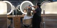 A hairdresser wearing protective mask and face shield uses a hair dryer on a customer's hair between acrylic walls set up for social distancing at a hair salon, as the city eases the restrictions imposed to control the spread of the coronavirus disease (COVID-19), in Sao Paulo, Brazil July 6, 2020. REUTERS/Amanda Perobelli  Foto: Reuters