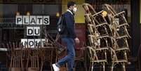 Homem caminha em frente a caf&eacute; fechado com as cadeiras empilhadas em Paris  Foto: EPA / BBC News Brasil