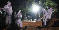 Coveiros com trajes de proteção fazem o sepultamento noturno no cemitério de Vila Formosa, em São Paulo  Foto: Amanda Perobelli / Reuters