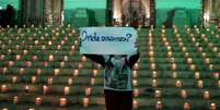Manifestante, com velas ao fundo, segura cartaz, onde está escrito: "Onde erramos?"  Foto: Reuters / BBC News Brasil