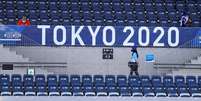 Espectadora caminha embaixo de placa da Tóquio 2020 no estádio onde é disputado o torneio olímpico do hóquei
24/07/2021 REUTERS/Siphiwe Sibeko  Foto: Reuters