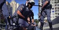 Imagem mostra grupo de policiais militares imobilizando jovem negro no asfalto  Foto: Imagem: Rovena Rosa/Agência Brasil / Alma Preta