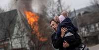 Homem e criança fogem de bombardeios em Irpin, na Ucrânia   Foto: Carlos Barria / Reuters
