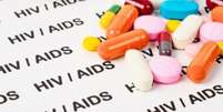 Imagem mostra comprimidos coloridos em cima de um letreiro contendo, em repetição, as palavras "HIV" e "Aids"  Foto: Imagem: Agência Brasil / Alma Preta