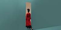 Mulher em um vestido vermelho passando por um buraco em uma parede azul  Foto: Getty Images / BBC News Brasil