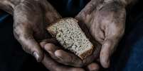Imagem enquadra duas mãos que seguram um pedaço de pão  Foto: Shutterstock / Alma Preta
