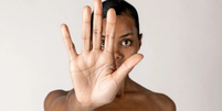 Mulher negra, em fundo branco, com a mão aberta para a câmera, simbolizando o basta de violência contra as mulheres  Foto: Imagem: Reprodução / Freepik / Alma Preta