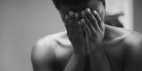 A imagem &eacute; em preto e branco e enquadra uma pessoa negra com as m&atilde;os no rosto  Foto: Reprodu&ccedil;&atilde;o/Nappy / Alma Preta