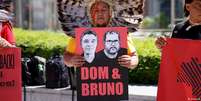 Indígena brasileiro segura cartaz com os rostos do indigenista Bruno Pereira e do jornalista britânico Dom Phillips durante manifestação em Bruxelas  Foto: DW / Deutsche Welle