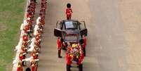 Soldados fardados colocam um caixão coberto com bandeiras e uma coroa em cima em um carro funerário  Foto: BBC News Brasil