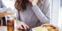 Comer dando atenção aos aparelhos eletrônicos podem prejudicar sua saúde  Foto: quintanilla / iStock