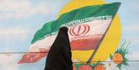 Mulher caminha em Terrã ante grafite com bandeira do Irã   Foto: Reuters