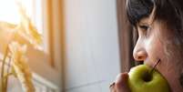 Imagem meramente ilustrativa de uma menina comendo uma fruta  Foto: Khamkor/ Unsplash