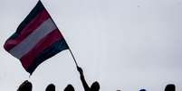 Imagem mostra a sombra de pessoas segurando a bandeira da população trans.  Foto: Gabriela Biló / Alma Preta