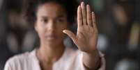 Imagem mostra o rosto de uma mulher negra desfocado e fazendo um sinal de "pare" com uma das mãos.  Foto: Arquivo CNJ / Alma Preta