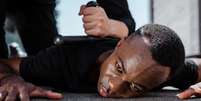 Imagem mostra homem negro no chão, sendo agredido e imobilizado por policial.  Foto: Reprodução / Alma Preta