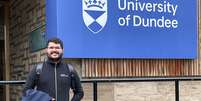 Dener Silva Miranda em frente ao logotipo da Universidade de Dundee, na Escócia, onde ele estudou pelo programa Ciência Sem Fronteiras  Foto: Arquivo pessoal / BBC News Brasil