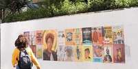 Mulher negra, de costas passando ao lado do mural a céu aberto, com 24 obras, pedindo uma ministra do STF negra.  Foto: Naetê Andreo / Alma Preta