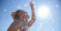 mulher jogando água na cabeça em dia de calor  Foto: Getty Images / BBC News Brasil