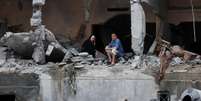 Palestinos sentam-se entre os escombros de um prédio residencial danificado, após os ataques israelenses, na Cidade de Gaza  Foto: Reuters / BBC News Brasil