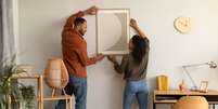 Imagem meramente ilustrativa de um casal arrumando um quadro na sala de casa Foto: Prostock-Studio / iStock