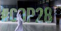 Homem passa na frente de letreiro com os dizeres COP28  Foto: Reuters / BBC News Brasil