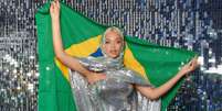 Imagem mostra Beyoncé com um vestido prateado e segurando a bandeira do Brasil.  Foto: Alma Preta