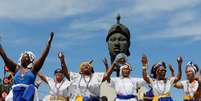 Na imagem, mulheres negras com vestimentas azul e branca, em frente a monumento de Zumbi dos Palmares  Foto: Alma Preta