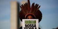 A imagem mostra uma mulher indígena segurando uma placa escrita "roubaram nossa terra, querem roubar nosso futuro", em manifestação contra o marco temporal.  Foto: Alma Preta