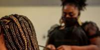 A imagem mostra uma mulher negra retinta fazendo tranças no cabelo de outra mulher.  Foto: Alma Preta