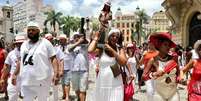 Imagem mostra pessoas em uma celebração religiosa na rua.  Foto: Alma Preta