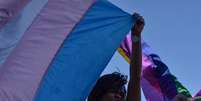 A imagem mostra uma pessoa negra segurando uma bandeira da população trans. Relatório revela que pessoas afetadas pelo racismo são maioria nos registros de assassinatos.  Foto: Alma Preta