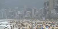 A imagem mostra uma praia do Rio de Janeiro cheia de banhistas na área e na areia.  Foto: Alma Preta