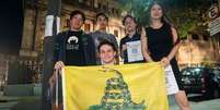 Membros do grupo Pibes Libertarios mostram uma bandeira de Gadsden, símbolo do libertarianismo  Foto: BBC News Brasil