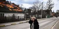 Uma mulher cobre o rosto com a mão enquanto está em frente a uma casa em chamas em Irpin, nos arredores de Kiev, 4 de março de 2022  Foto: Getty Images / BBC News Brasil