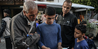 Dois homens e dois meninos em uma rua em Gaza olham para um folheto com alerta de evacuação emitido pelas FDI  Foto: Getty Images / Anadolu / BBC News Brasil