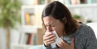 Mulher adulta doente tossindo cobrindo boca com tecido em casa  Foto: Pheelings Media/iStock