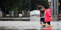 homem ajudando mulher a andar por rua alagadaágua  Foto: Reuters / BBC News Brasil