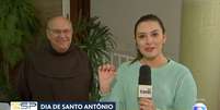 Isabela Sabéllico segurando a medalha de Santo Antônio, ao lado do frei Gilberto Piscitelli, responsável pelo 'bolo do desencalhe'  Foto: Reprodução/TV