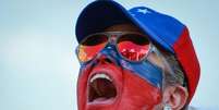 Manifestante com o rosto pintado de vermelho e azul, usando óculos e boné também nas cores azul e vermelho  Foto: Getty Images / BBC News Brasil