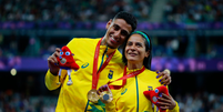 Gabriel Garcia e Jerusa Geber estão com a medalha de ouro no peito e seguram a Phryge, a mascota dos Jogos. Ele a abraça, vestindo uniforme amarelo, com detalhes em verde   Foto: Wander Roberto/CPB / Olimpíada Todo Dia